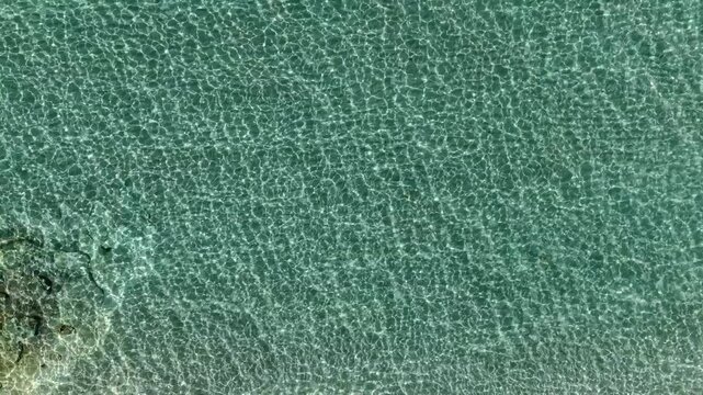 Transparent turquoise water reflecting sunlight with shimmering ripples, tropical seas in natural light, Simos beach, Elafonisos island, Drone shot