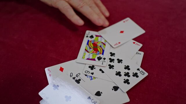 An elderly person places a playing card onto a pile during a social game, supporting concentration, decision-making and mental stimulation. Close up.