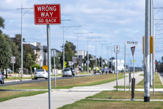 A regulatory sign reading "WRONG WAY GO BACK" at a divided dual-carriageway road at the intersection bordered by residential houses in Truganina, suburb of Melbourne, Australia.