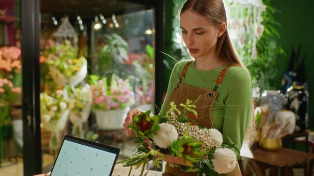 Young adult Caucasian female florist arranging flower bouquet while talking to colleague at counter. Ideal for small business marketing and local retail service promotion