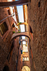 Fototapeta premium Tall narrow alley in Siena with brick facades and a deep perspective leading through the old town. A classic scene of Tuscan medieval architecture.