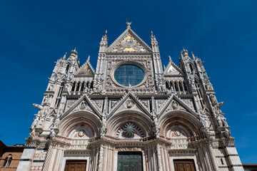 Fototapeta premium Front view of Siena Cathedral with its iconic facade under a clear blue sky. The composition highlights the symmetry and elegance of the historic building.