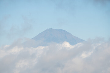 Fototapeta premium Mountain peak emerging from behind a layer of clouds. A mountain with a layer of clouds in front of it.