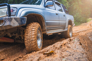 Close-up of a 4x4 offroad vehicle with all-terrain tires powering through a muddy road. Mud splash, wheel spin, deep tread, traction, overlanding adventure, rugged terrain, outdoor driving. © Tinnakorn