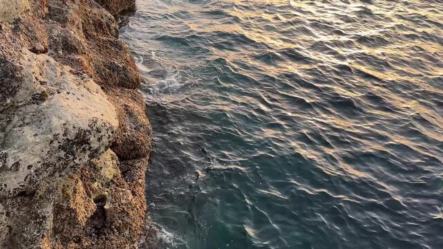 Smooth camera movement from coastal rocks toward the open Atlantic Ocean at sunset, accompanied by gentle water splashing and warm golden evening light.