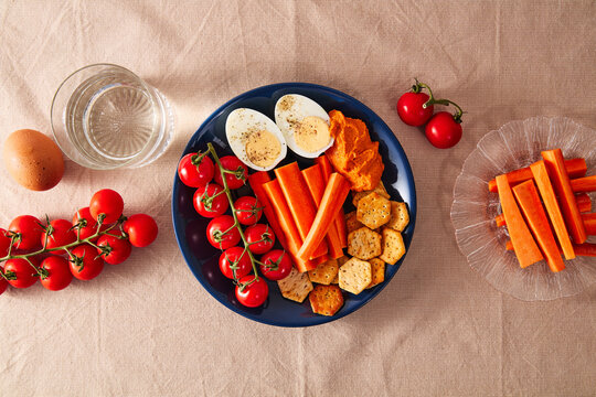 Healthy snack platter with boiled eggs, carrots, cherry tomatoes, crackers, and dip on a linen tablecloth