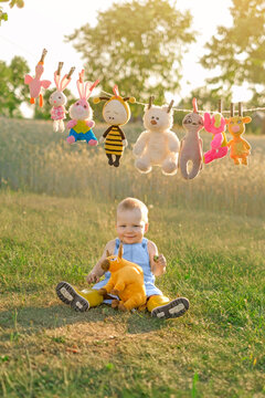 A little one-year-old boy is sitting on the grass in a park, surrounded by a variety of toys that are drying after being washed.