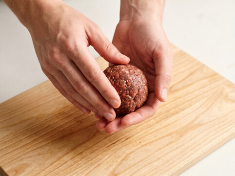 Hands shaping a raw ground meatball on a wooden cutting board