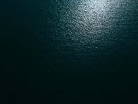 Aerial top down view of a blue sea water surface with sun reflection