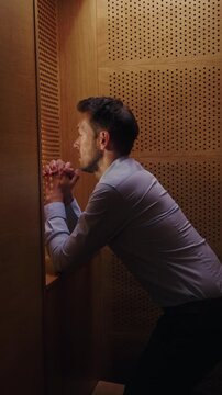 Man penitent, in a confession booth, confessing sins to a priest to receive absolution and spiritual healing. Faith concept.