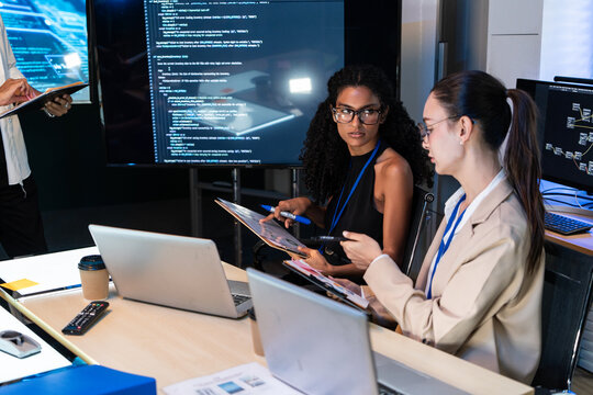 Two businesswoman talk share creative idea with laptop computer while software engineer team work together analyze programming code screen at office