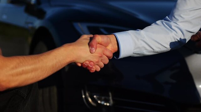 Male hand giving key of car to buyer of electric automobile outdoor. Handshake between salesman and new owner of modern auto after successful deal. Concept of buy or rent car. Slow mo