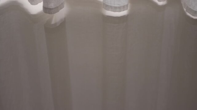 Curtain hem hanging at the top with sunlight leaking through, casting long vertical reflection of swaying fabric on a glossy surface, abstract interior background, cinematic B-roll.