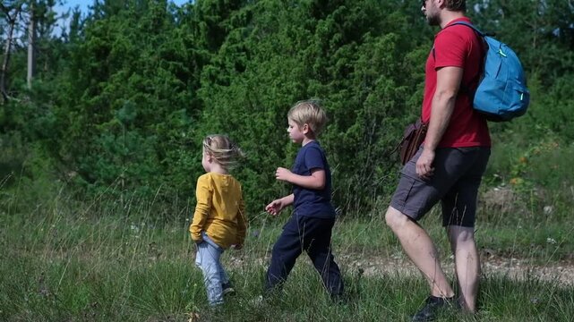 Father walking with his two little children in summer forest. Dad hiking with son and daughter on green grass field, weekend outdoor adventure activity theme. Active Family Lifestyle. Nature Escape