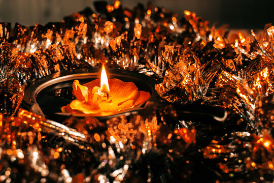 Golden Diwali Diya lamp with flame, floating in a pool of golden tinsel for traditional festival decoration