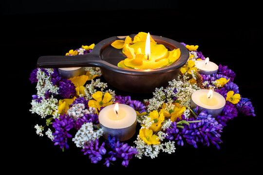 Diwali floral arrangement with burning tea light candles and floating yellow flower in a black bowl against black background