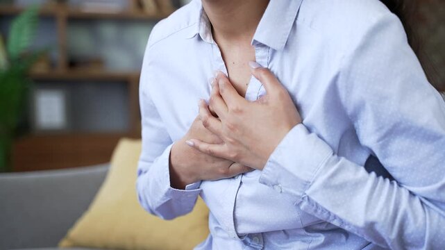 Close up woman has heart attack while sitting on sofa in living room at home. Sick adult female suffers from tension in chest and massages sore spot with her hand. She needs urgent medical attention