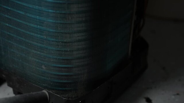 Close-up of a dusty air conditioner condenser coil in low light, Metal fins and a dark hose in an indoor maintenance