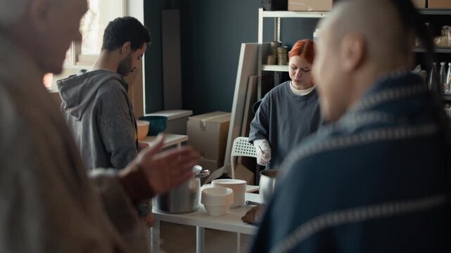Young adult Caucasian female volunteer stirring hot soup in pot at community shelter. Footage is ideal for charity campaigns, humanitarian aid promos, and social responsibility advertisements