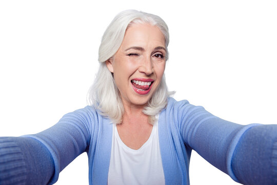 Close up portrait of happy cheerful delightful charming beautiful flirty mature lady granny grandma, she is giving a wink, showing a tongue and taking a selfie on vacation, isolated on gray background