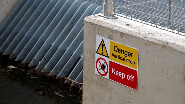 Danger vertical drop keep off sign, warning notice on industrial water infrastructure, safety caution placard on concrete wall at construction site drainage channel