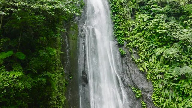 Aerial view of Pulang-Tubig Falls in green forest in slow motion. Waterfall in the tropical mountain jungle. Negros, Philippines.
