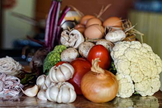 Natural assortment of fresh vegetables and eggs on rustic kitchen table. Organic ingredients for healthy cooking, farm to table concept, raw food preparation background.