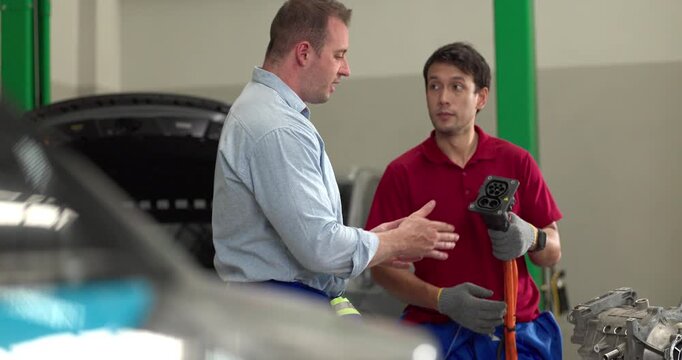 Senior engineer and technician inspecting electric vehicle motor component with high voltage cable
