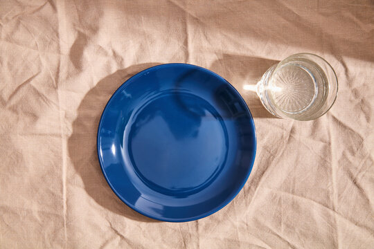 Empty blue ceramic plate and glass of water on linen tablecloth