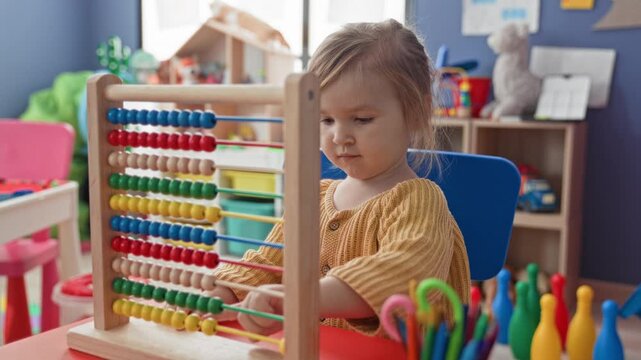 Blonde girl sliding beads on an abacus with her hand in a building preschool classroom; early learning concentration.