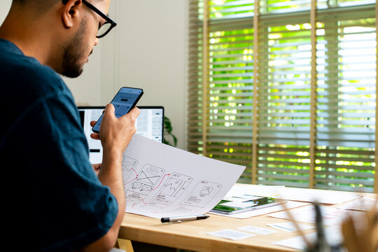UX UI designer working on wireframes for a website and mobile app prototype, surrounded by sketches of user-flow and design tools, in concept of website and mobile application design concept.