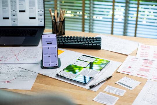 UX UI wireframes for a website and mobile app prototype, surrounded by sketches of user-flow and design tools, in concept of website and mobile application design concept.
