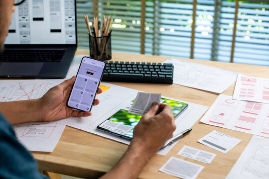 UX UI designer testing prototype on a phone, working on wireframes for a website and mobile app prototype, in concept of website and mobile application design concept.