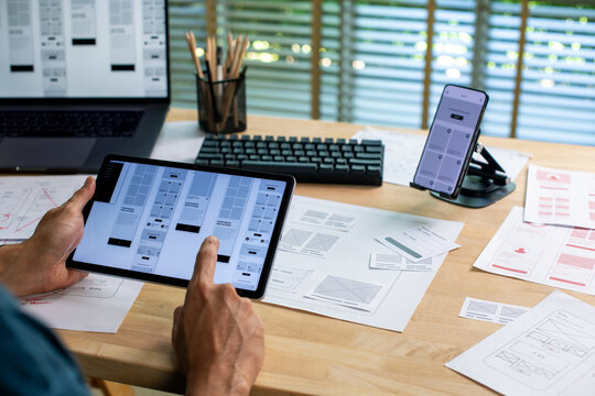 UX UI designer working on wireframes for a website and mobile app prototype, surrounded by sketches of user-flow and design tools, in concept of website and mobile application design concept.