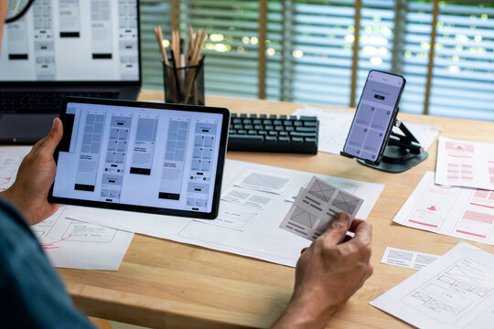 UX UI designer working on wireframes for a website and mobile app prototype, surrounded by sketches of user-flow and design tools, in concept of website and mobile application design concept.