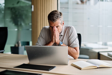 Fototapeta premium Portrait of a young businessman or a young entrepreneur or a student having a headache and being under pressure and stress working on tablet or laptop computer working in office