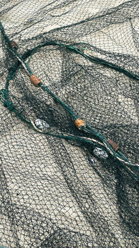 Fishing net with floats lying on sandy beach, textured marine background