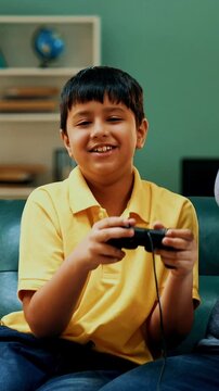 Indian Asian father son playing video game sitting on a sofa, both intensely focused on gaming competition, father wins and playfully teases son, sharing a fun and joyful bonding moment at home