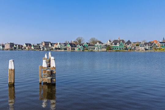 Zaandam, Netherlands: A picturesque row of traditional green wooden houses lining the waterfront of the Zaan river with mooring poles in front.