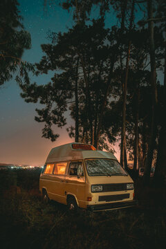 Vintage Campervan Glowing at Night Under Starry Sky in Pine Forest