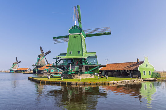 Zaandam, Netherlands: The historic green windmill De Poelenburg standing by the water under a clear blue sky at Zaanse Schans.