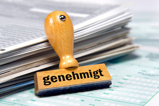 Ein Papierstapel mit Antr&auml;gen und einem Holzstempel mit Aufdruck - genehmigt