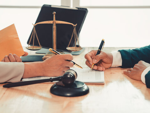 Lawyer holding pen and explaining legal contract terms on clipboard to client during consultation in law firm.