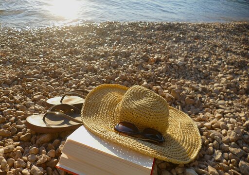 Book on the beach and woman straw hat with glass and flip flop sandals, summertime accessories by the sea