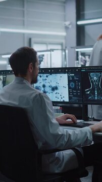 Vertical Screen. Male Scientist Types on Keyboard While Studying Molecular Structures and MRI Scans  in Advanced Biotechnology Lab. Physician Researches Drug Development for Disease Treatment.
