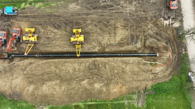 Aerial view of a major pipeline construction project. Heavy machinery including excavators and pipelayers install a new gas line in a rural field. Industrial energy infrastructure development.