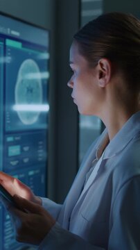 Vertical Screen. Determined Caucasian Woman Scientist Taps Digital Tablet While Reviewing Brain Mri Scan on Glowing Monitor in Medical Lab. Physician Explores Neurology Data for Drug Development.