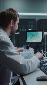 Vertical Screen. Male Scientist Studies Digital Microscope Display Showing Cell Sample While Typing on Keyboard in Modern Medical Research Laboratory. Researcher Conducts Drug Development Analysis.