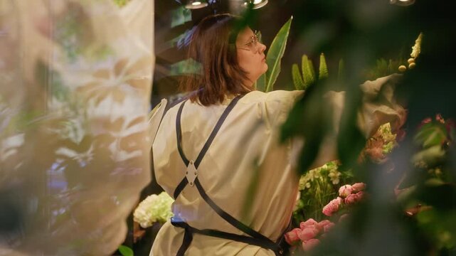 Young adult Caucasian female florist arranging fresh pink hydrangeas in flower shop display window. Footage perfect for small business promotion and local retail marketing campaigns