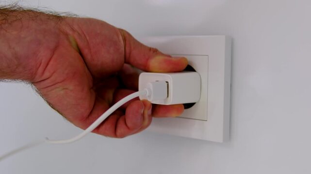 Male hand plugging USB power adapter into double white wall outlet for charging electronic devices in modern home or office close up technology video